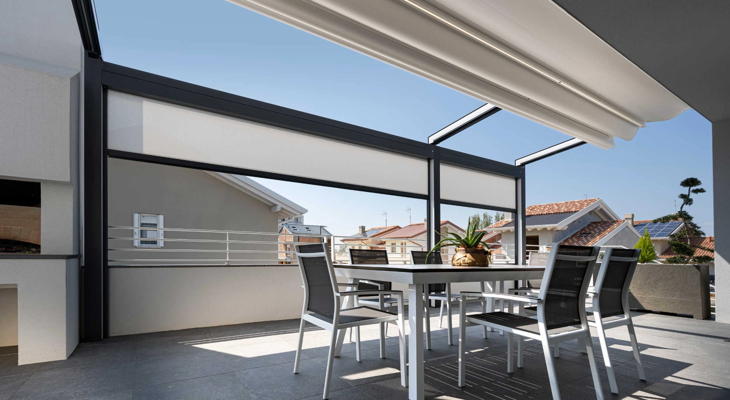 Zunanja terasa z belo pergolo in senčili, opremljena z moderno jedilno garnituro ter pogledom na strehe bližnjih hiš.