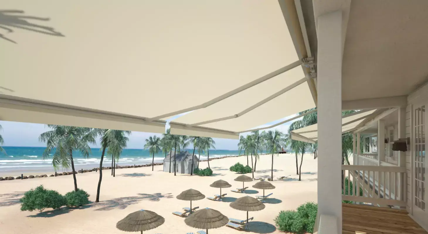 Zložljive bež tende nad teraso s pogledom na peščeno plažo, palme in morje.