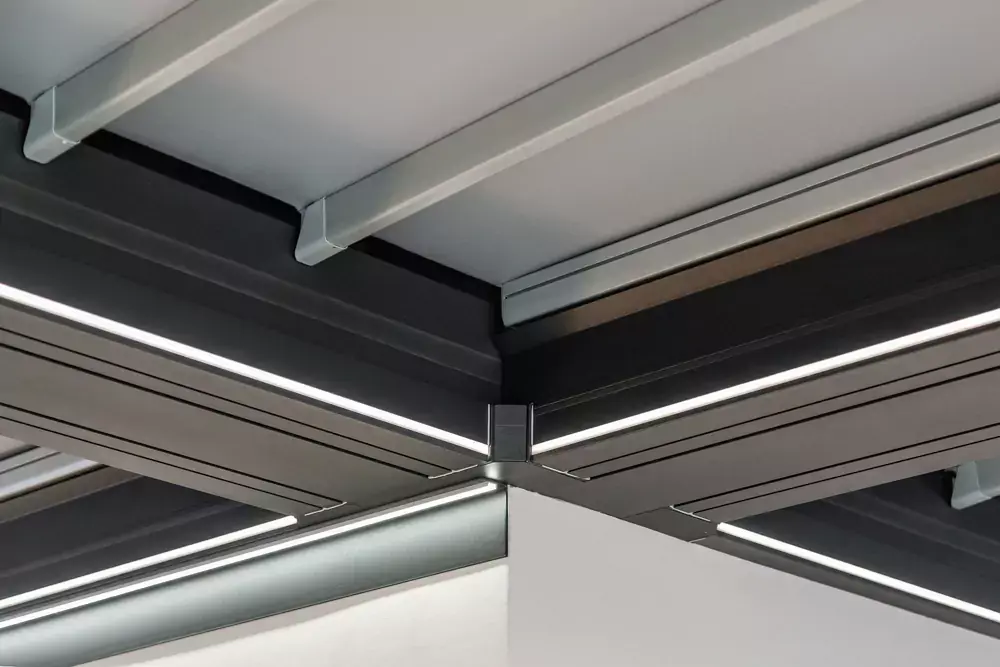 Detajl stropa moderne pergole z integrirano LED osvetlitvijo in aluminijasto konstrukcijo v temni barvi.