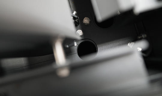 Makro posnetek notranjega mehanskega dela pergole z vidnimi vijaki, kovinskimi spoji in odprtino za sestavne elemente.