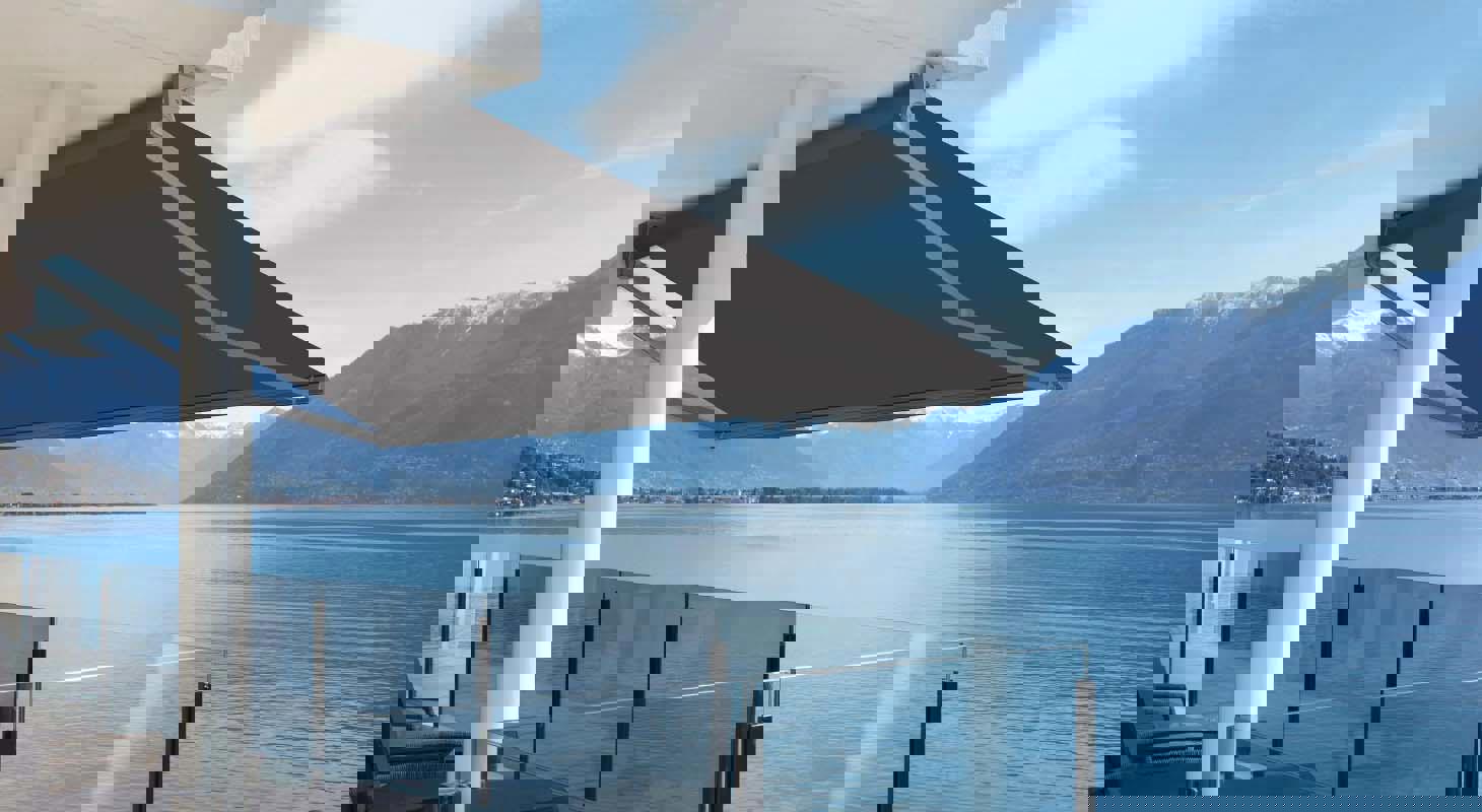 Moderna črna tenda na terasi z razgledom na jezero in gore, s stekleno ograjo v ospredju.