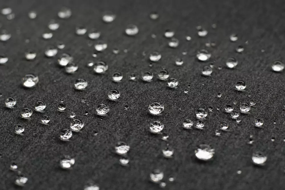 Kapljice vode na temni vodoodbojni tkanini, ki prikazujejo odpornost materiala na dež in odvečno vlago.