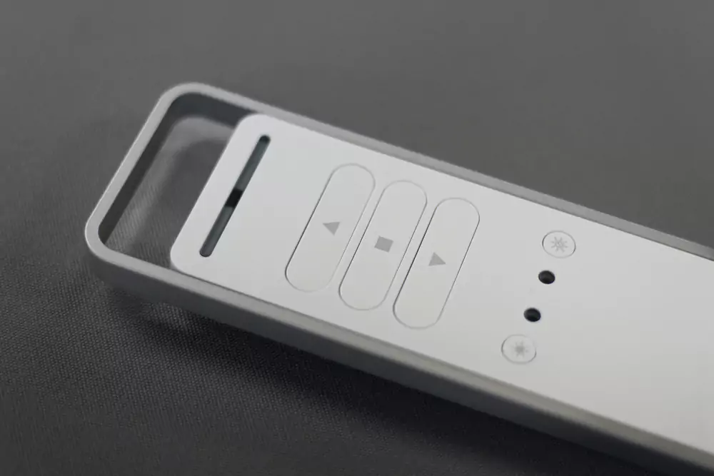 Daljinski upravljalnik za nadzor senčil in osvetlitve, s sodobnim minimalističnim dizajnom v sivi barvi.