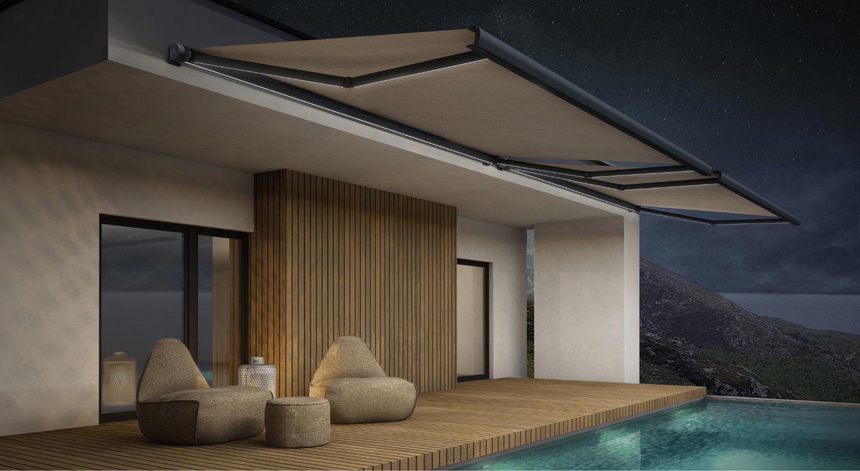 Terasa z bazenom ponoči, osvetljena bež tenda z LED lučmi, nameščena na strop sodobne hiše ob hribovitem obalnem območju.